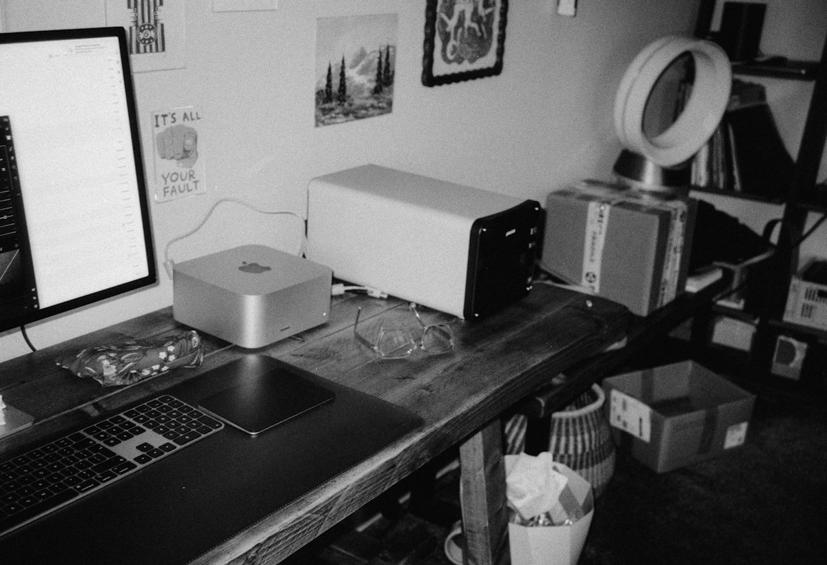 A desk with computers, fan, and storage shelves.
