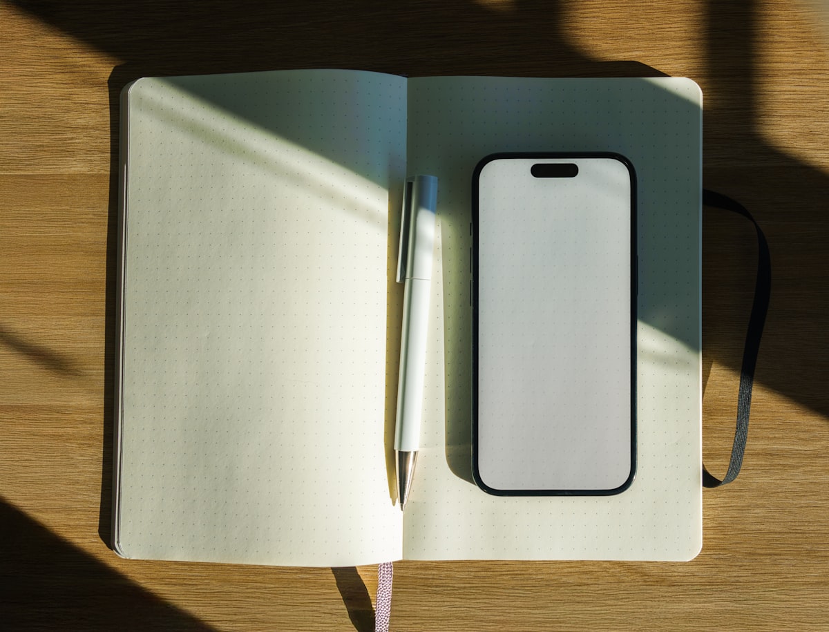 Notebook with pen and smartphone on wooden table.