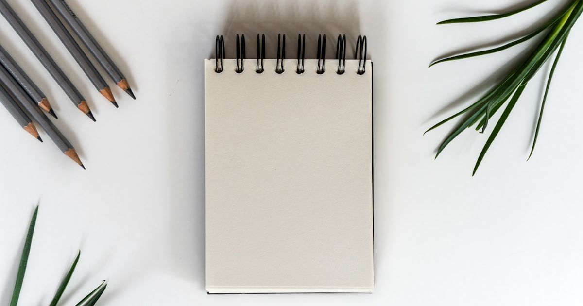 Pencils and a notepad with green leaves on white