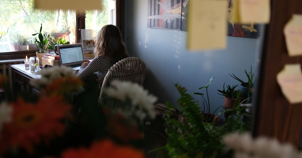 Woman working on laptop at a desk with plants.