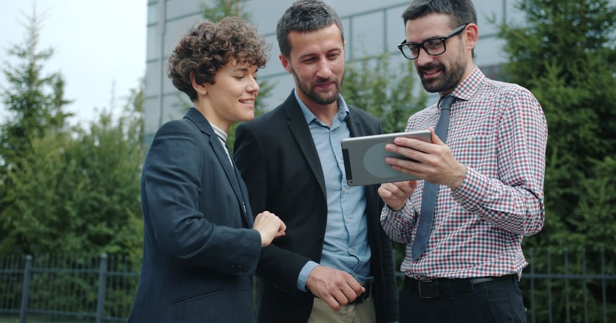Three business people looking at a tablet outside.